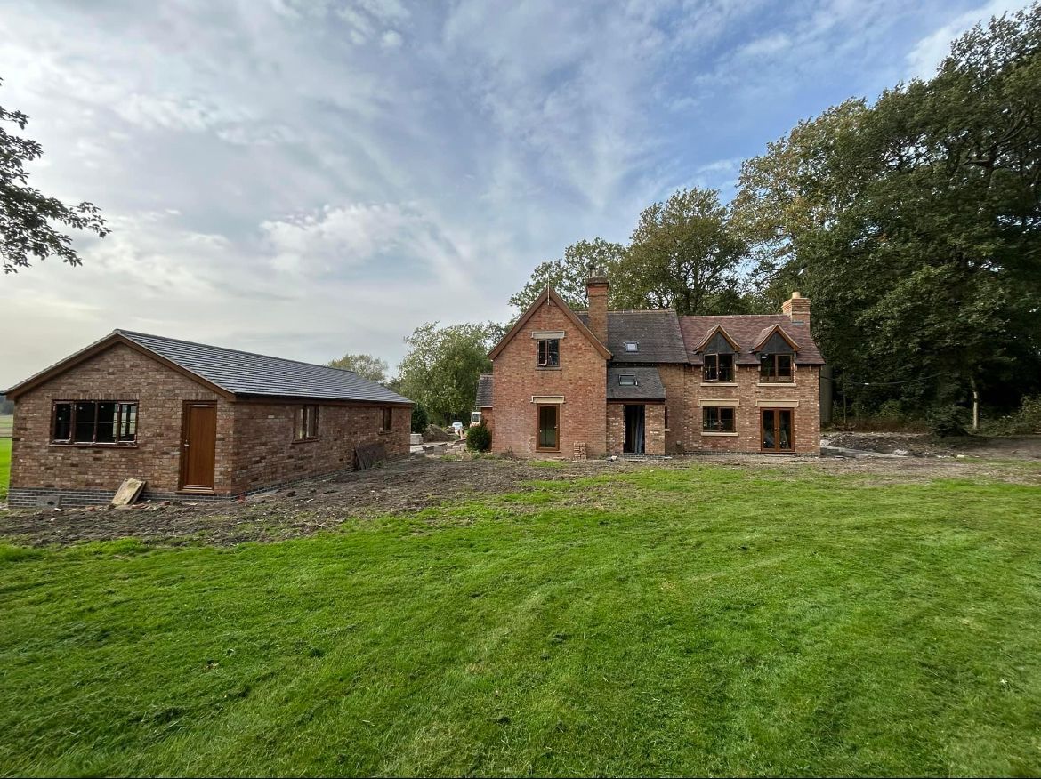 A large brick house is being built in the middle of a lush green field.