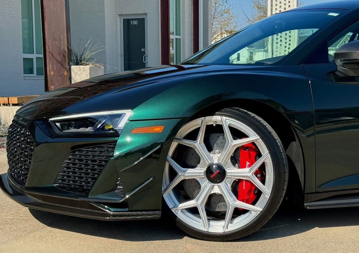 A green sports car with red brake calipers is parked in front of a building.