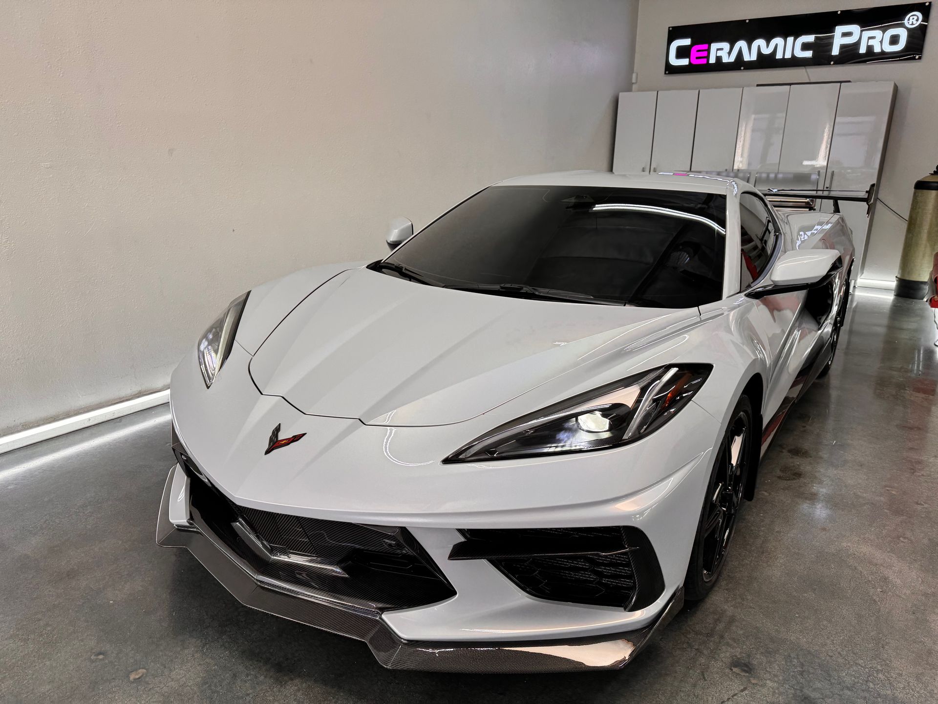 A white corvette is parked in a garage next to a sign that says ceramic pro.