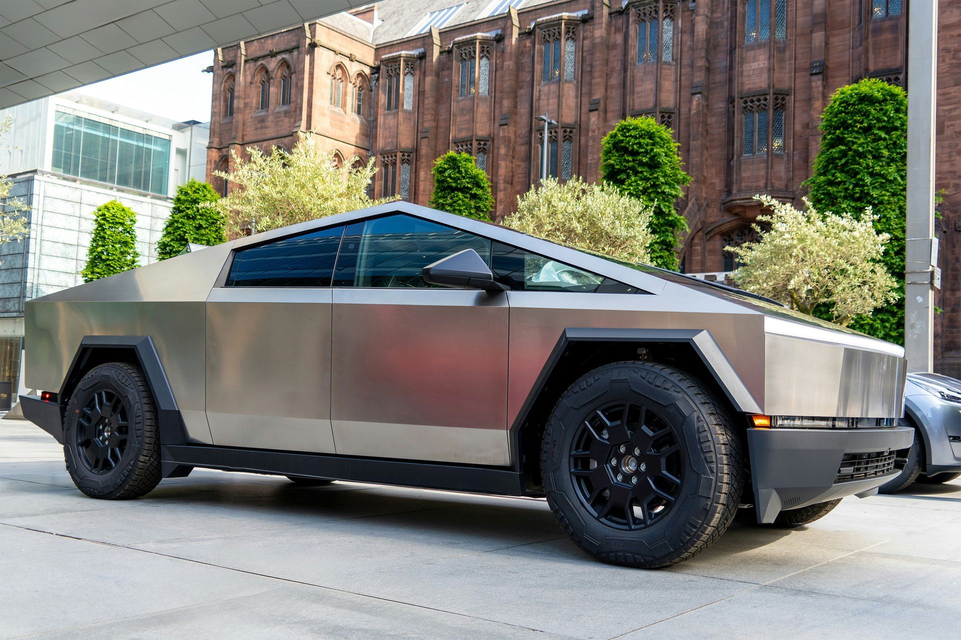 A silver tesla cybertruck is parked in front of a brick building.