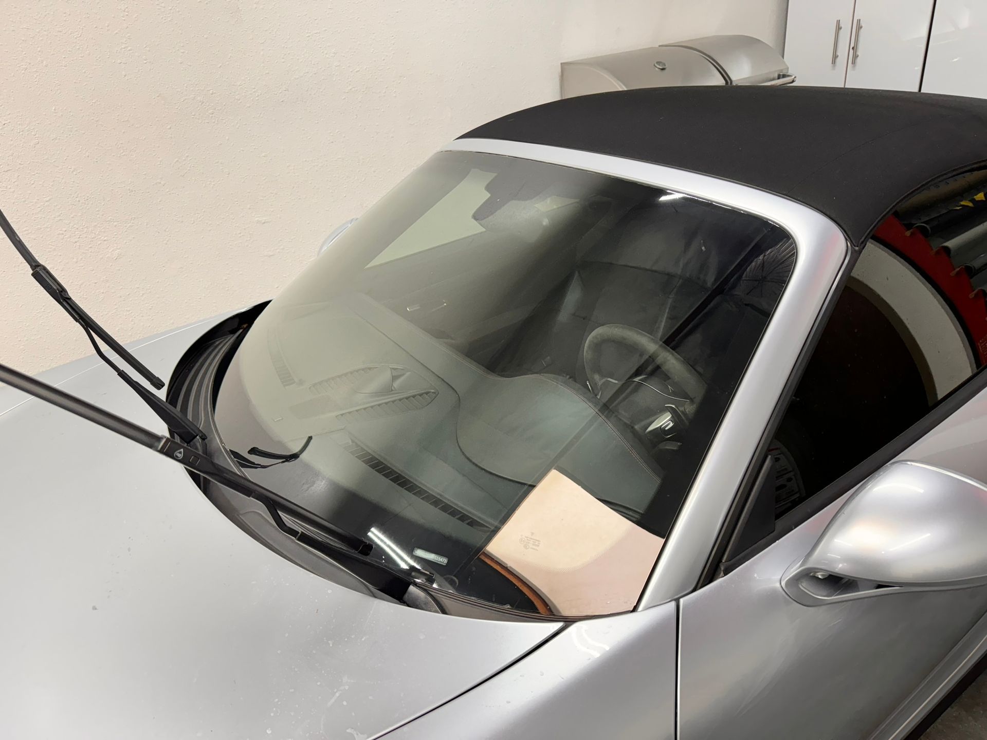 A silver sports car with a black top is parked in a garage