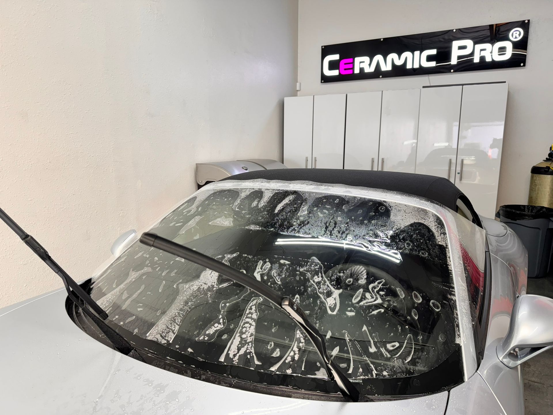 A silver sports car with a black top is parked in a garage