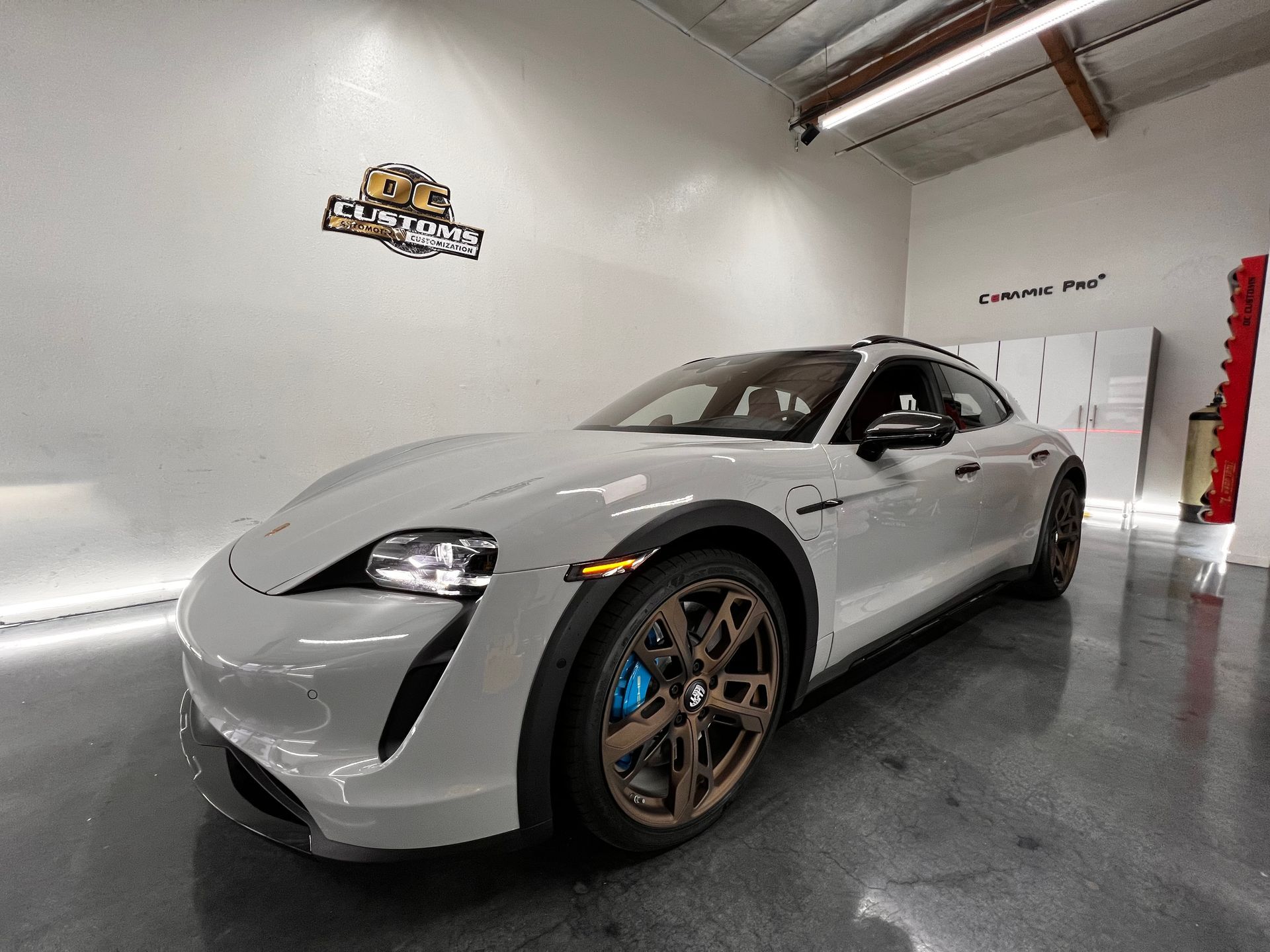 A white porsche taycan is parked in a garage.