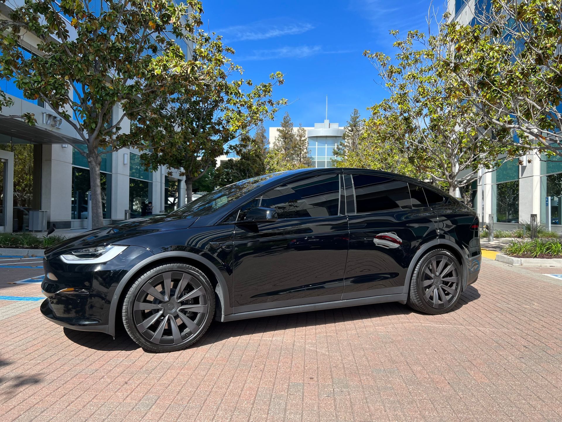 A black tesla model x is parked in a parking lot in front of a building.