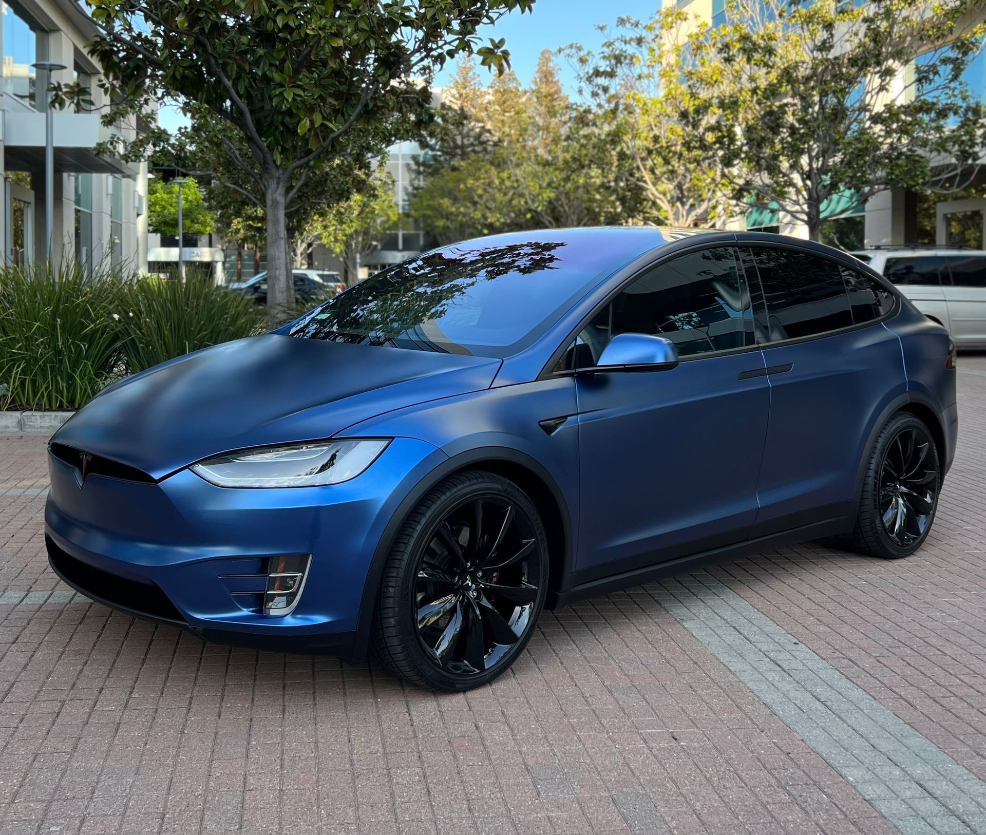 A blue tesla model x is parked on a brick sidewalk.
