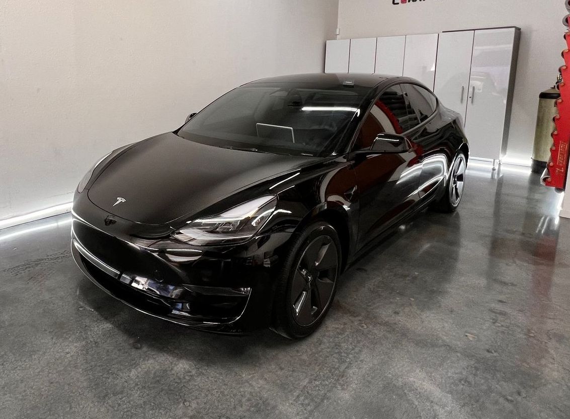 A black tesla model 3 is parked in a garage.