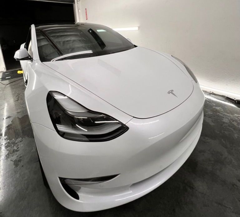 A white tesla model 3 is parked in a garage.