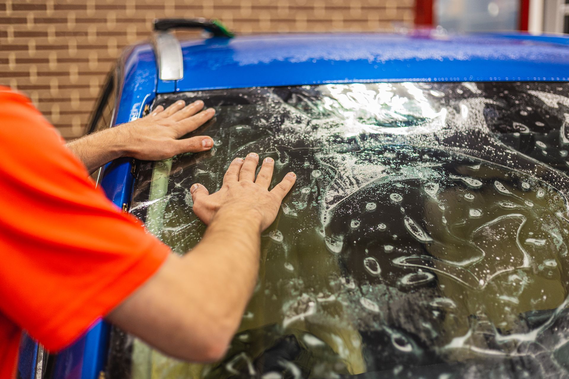 A man is applying tinted window film to a blue car.