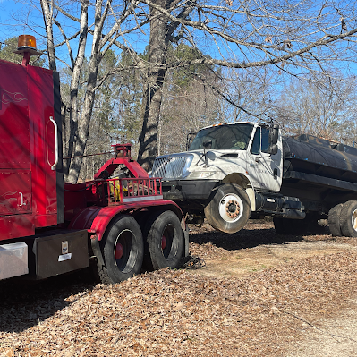 A red semi truck is towing a dump truck on a dirt road.