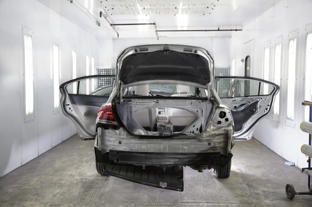 A car is being painted in a paint booth with its doors open.