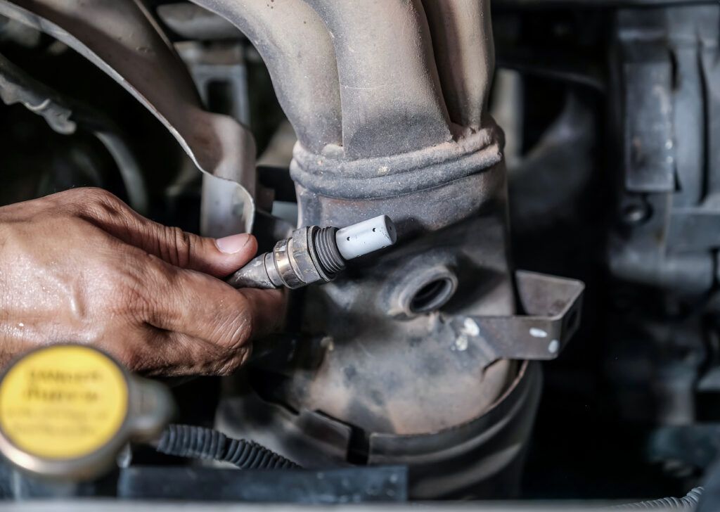 A person is fixing a car exhaust pipe with a wrench.
