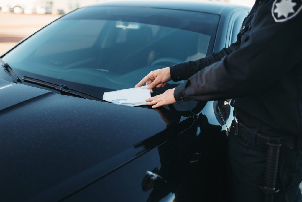 A police officer is giving a ticket to a driver in a black car.
