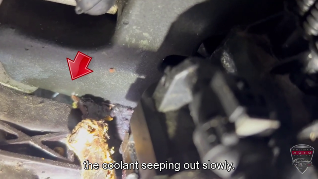 A close up of a car engine with a red arrow pointing to the coolant coming out slowly.