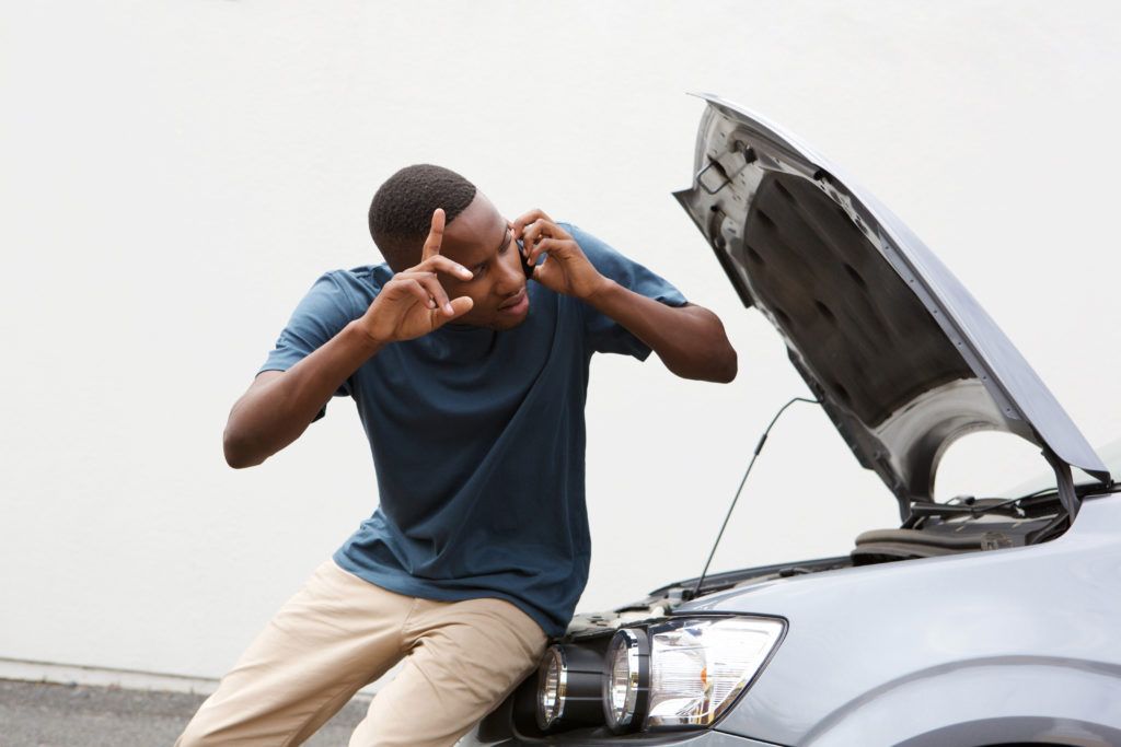 A man is sitting on the hood of a broken down car