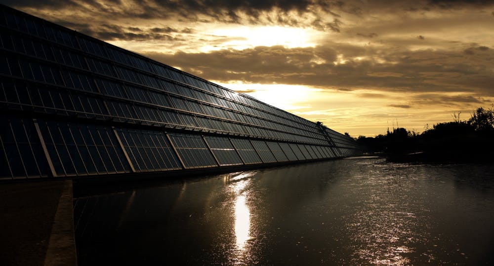 Een rij zonnepanelen naast een watermassa bij zonsondergang.