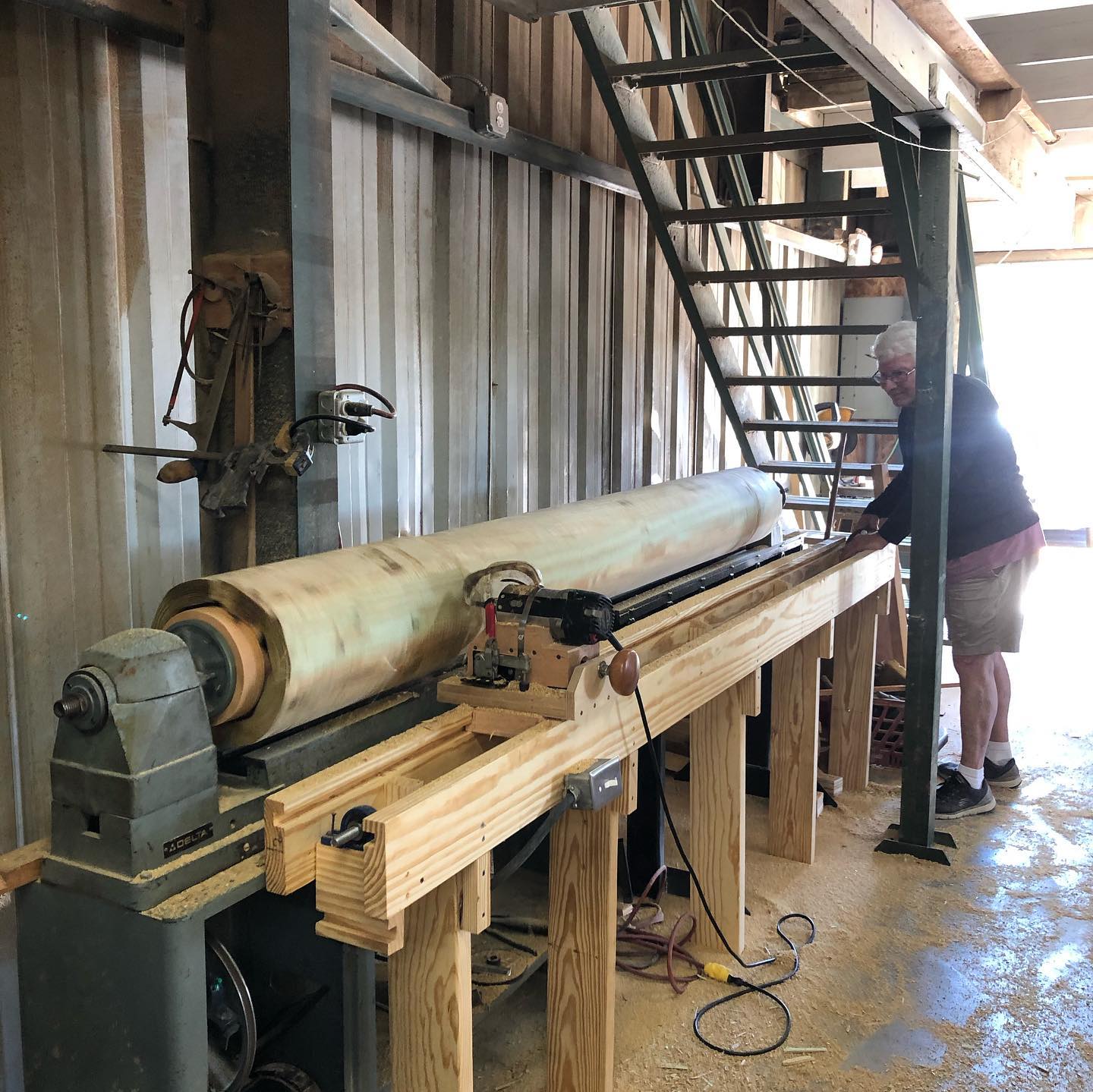 A man is working on a wooden lathe in a workshop.