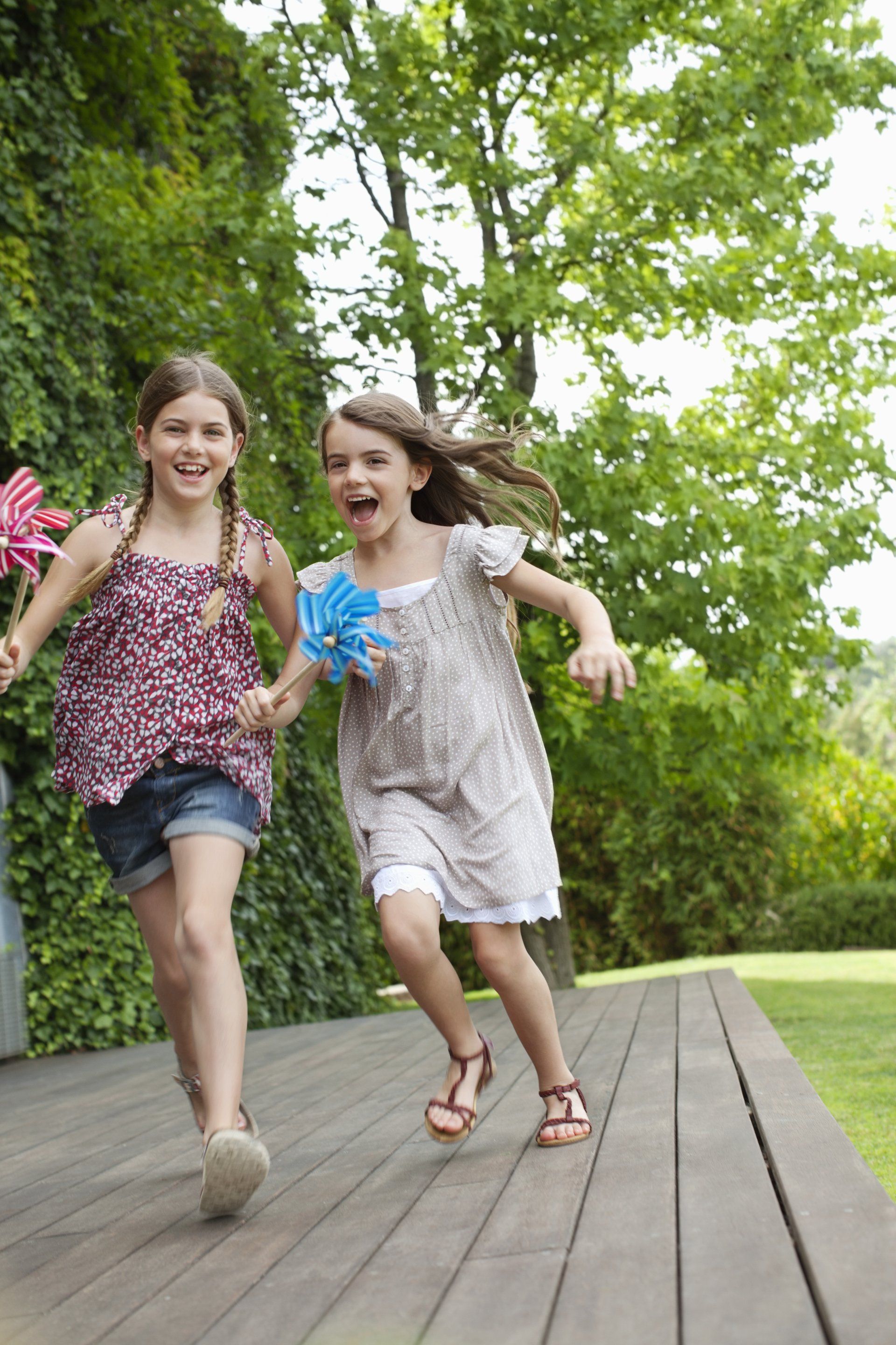 Two young girls are running on a wooden deck holding hands.