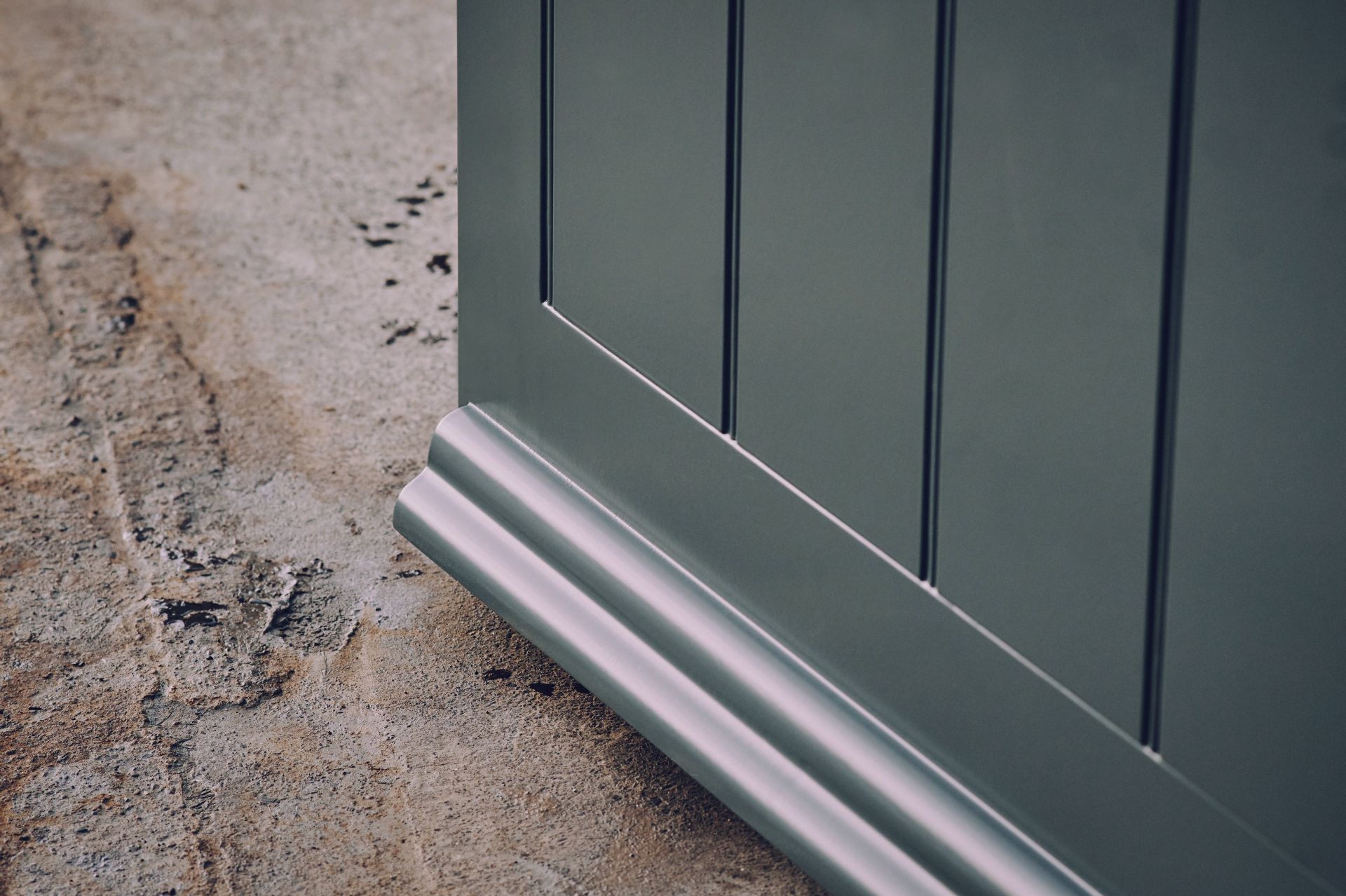 A green door with a silver trim is sitting on a concrete floor.