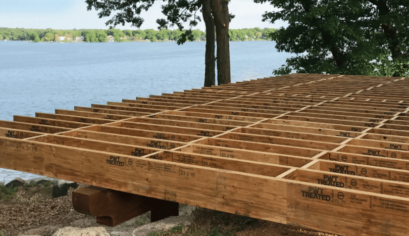 A wooden deck with a bench in the background and trees in the background.