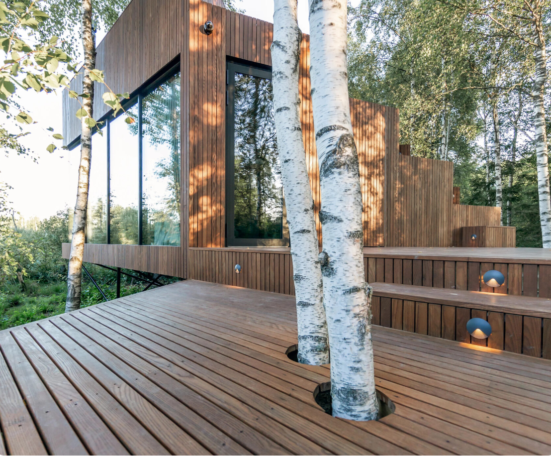 A wooden deck with a house in the background and trees in the foreground.