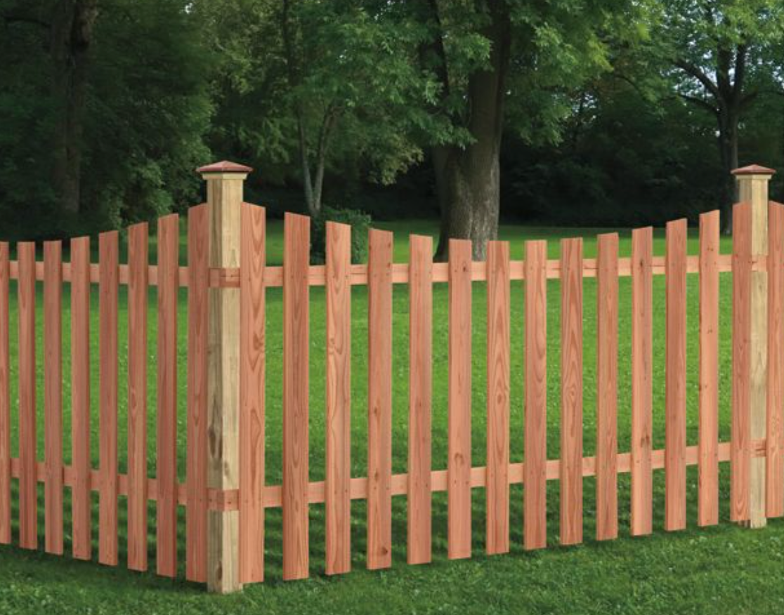 A wooden picket fence is in the middle of a lush green field.