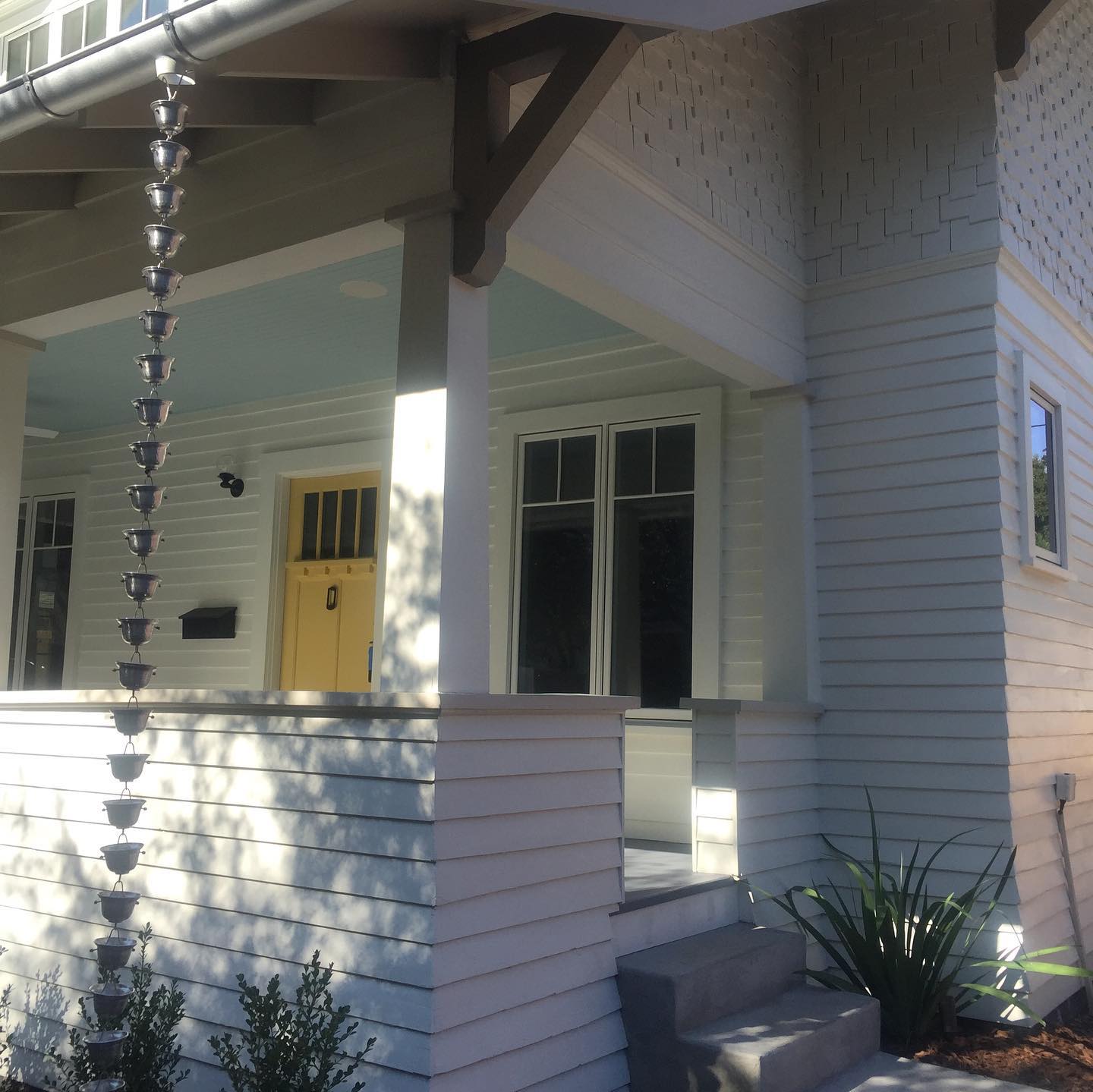 A white house with a yellow door and a rain chain