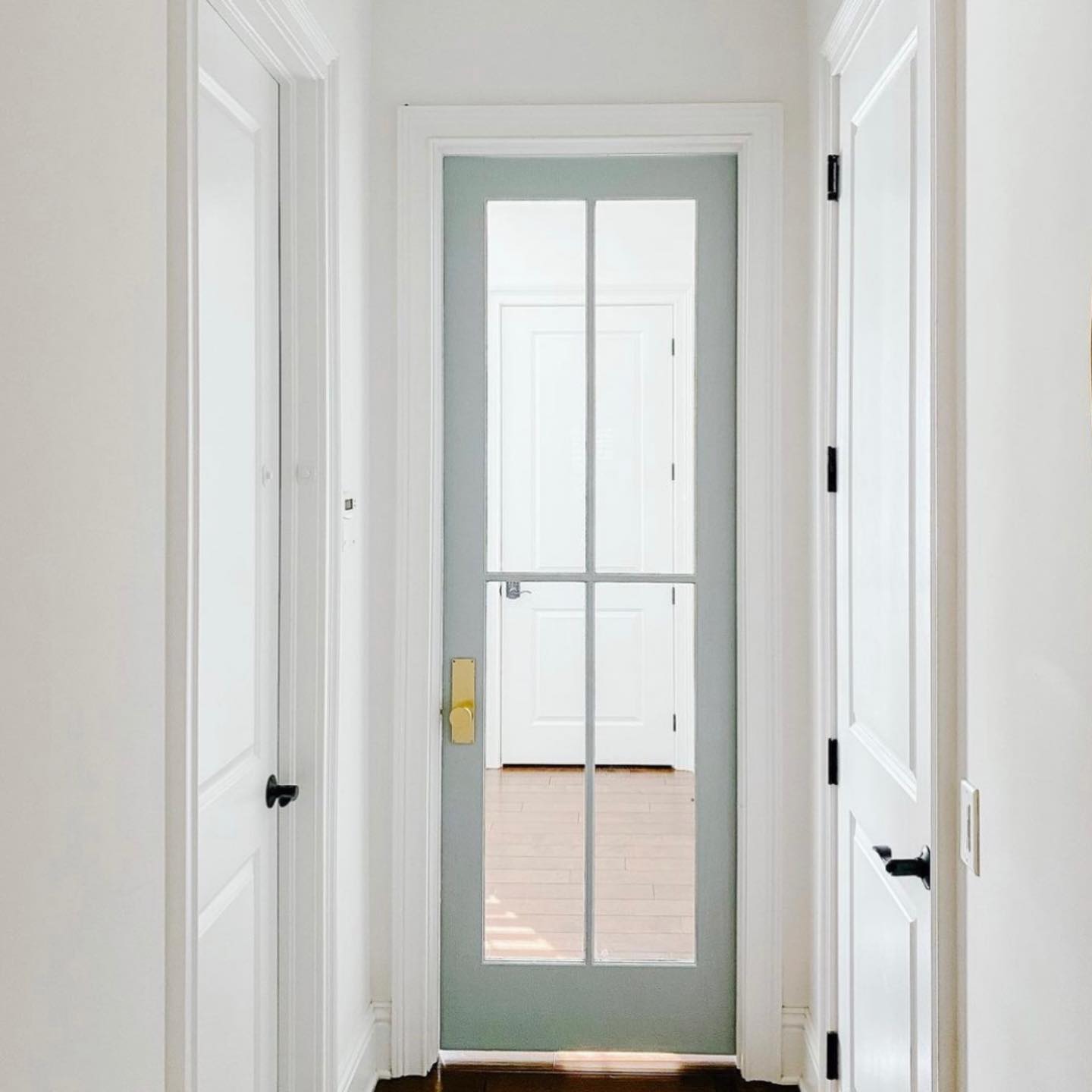 A hallway with a glass door and white walls.