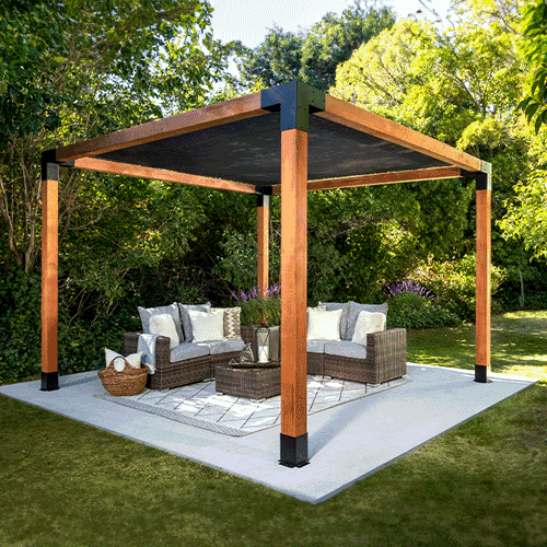 Wooden pergola over patio furniture in a garden; black shade and corner accents, on a concrete patio.