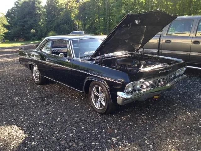 Black 1966 Chevrolet Chevelle with hood up, chrome wheels, parked on gravel. | 