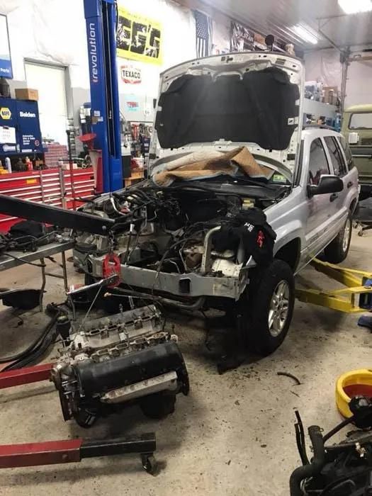 Jeep Grand Cherokee in a repair shop with the engine removed; hood open, parts scattered. | Dave Muller Automotive & Trailer