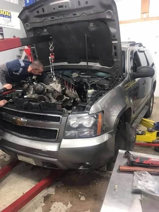 A mechanic using a hoist to remove an engine from a gray Chevy Tahoe in a garage. | Dave Muller Automotive & Trailer