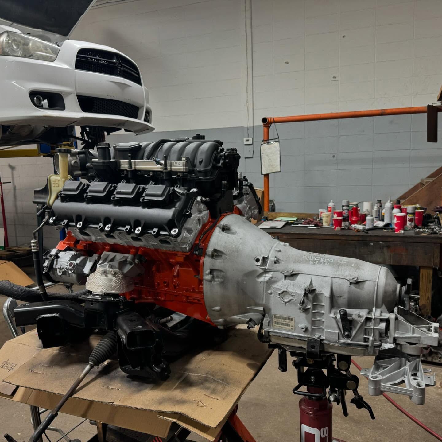 Engine and transmission assembly on a stand in a garage; a white car is in the background. | Dave Muller Automotive & Trailer