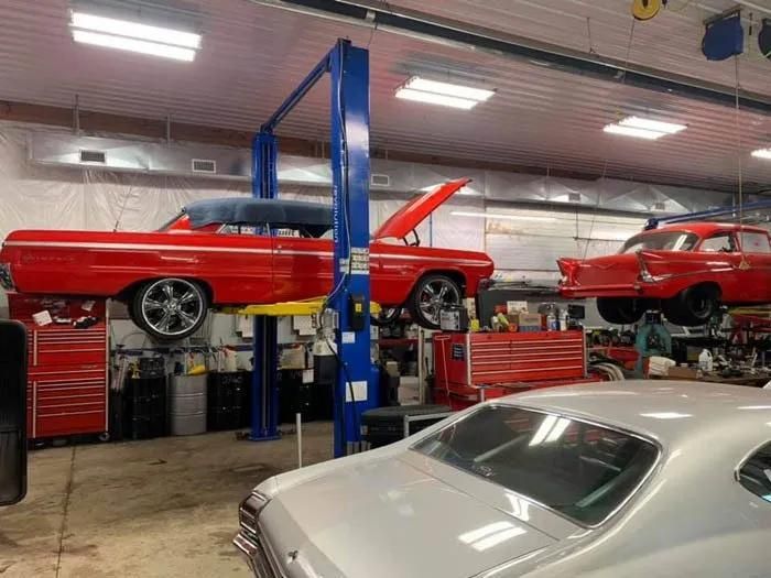 Classic red cars being worked on in a well-lit auto shop, one on a lift. | Dave Muller Automotive & Trailer