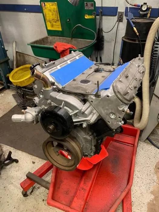 An LS engine on a red engine stand, in a garage. Blue tape covers the engine's tops. | Dave Muller Automotive & Trailer