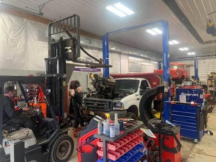 Mechanics working in a truck repair shop, with a forklift and vehicles on lifts. | Dave Muller Automotive & Trailer