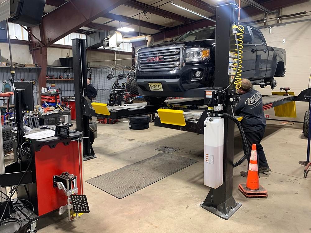 A black truck on a lift in a garage, a mechanic working, and tools are visible. | Dave Muller Automotive & Trailer