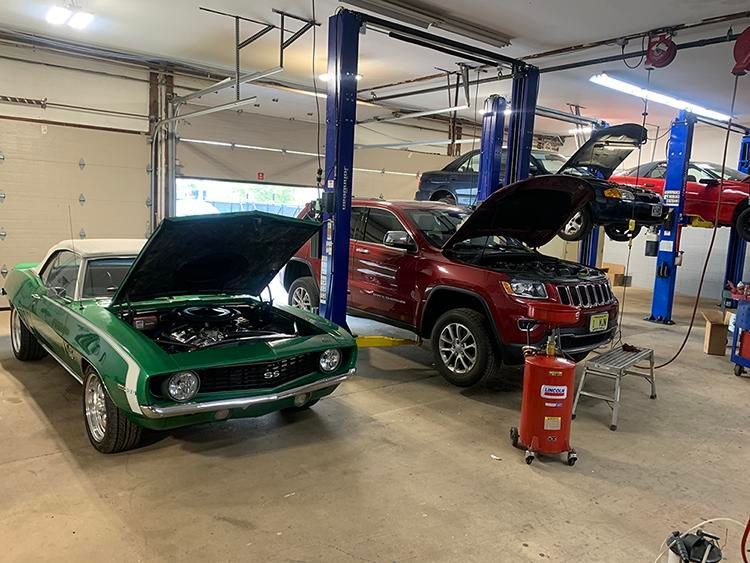 Classic green car and red SUV with open hoods in a garage, multiple cars on lifts. | Dave Muller Automotive & Trailer