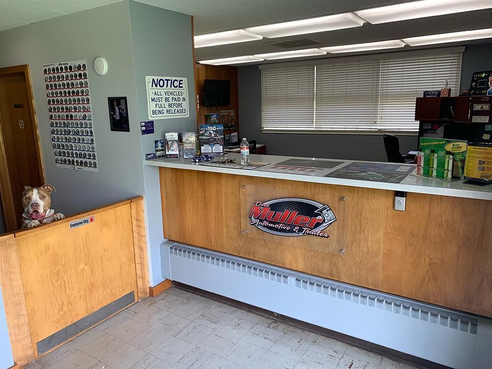 Dog at a car service desk, peeking over a wooden gate. The counter has a logo; a sign and a door are also visible.