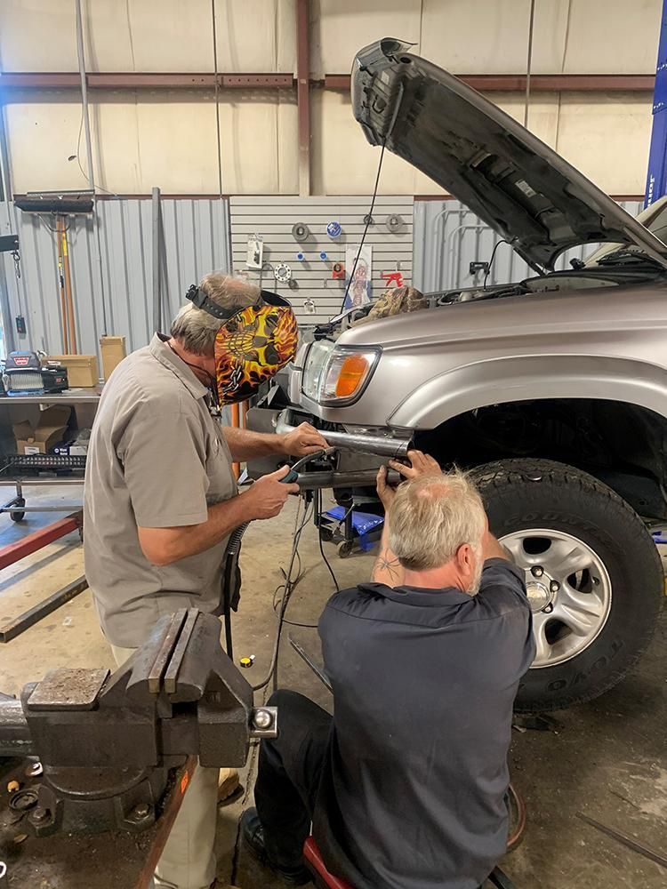 Two men working on a silver car in a garage; one is welding. | Dave Muller Automotive & Trailer
