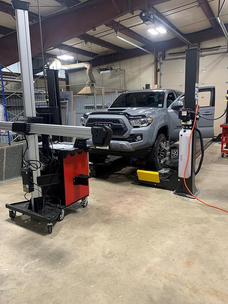 Gray truck on a lift in a garage being serviced by alignment equipment; red and black. | Dave Muller Automotive & Trailer
