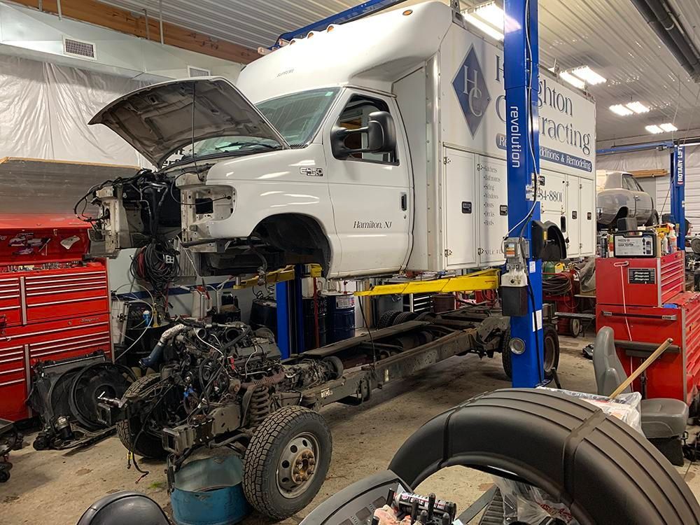White work truck on a lift in a repair shop, with the engine and front body removed. | Dave Muller Automotive & Trailer
