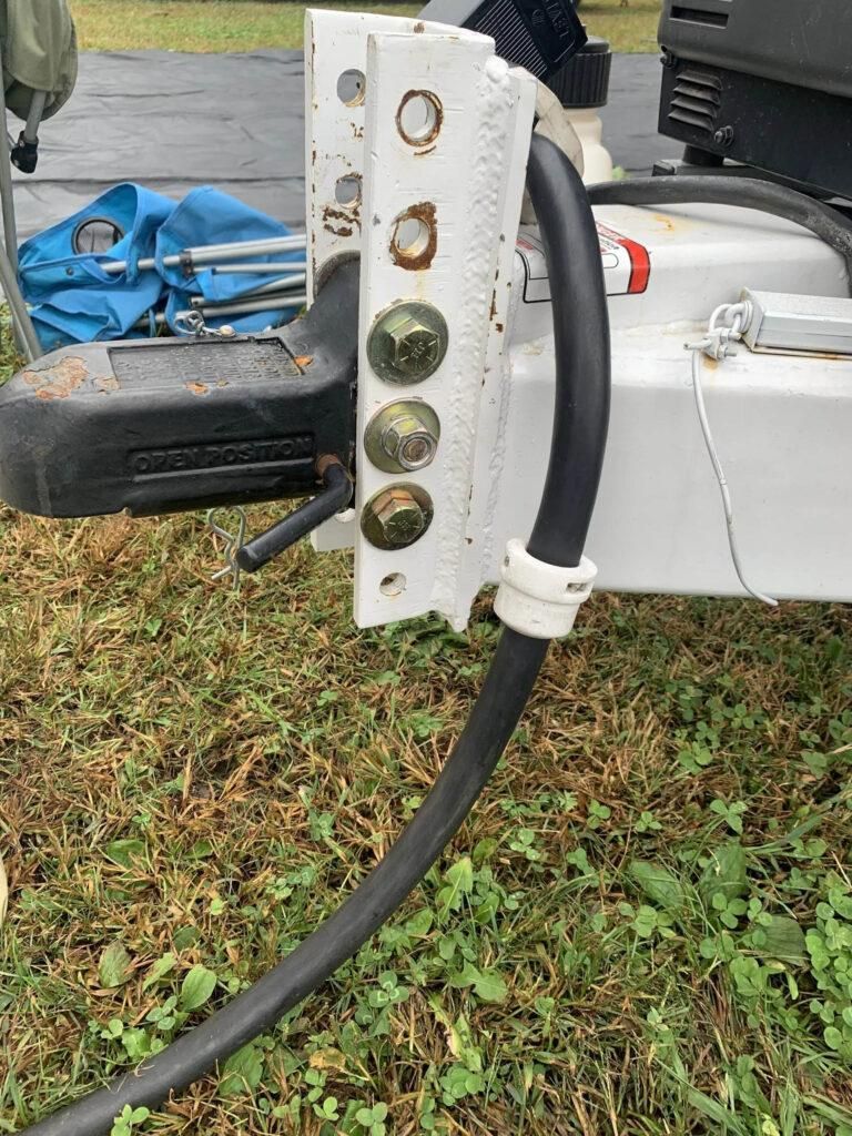 Trailer hitch with bolts, a black hose, and white metal bracket attached to a trailer. | Dave Muller Automotive & Trailer