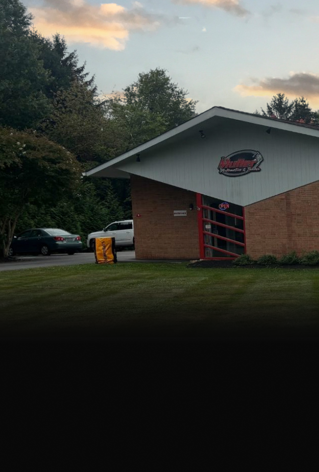 Building with red trim and a logo, parked cars, green grass, and trees. | Dave Muller Automotive & Trailer