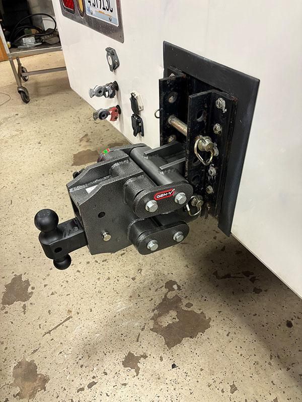 A heavy-duty trailer hitch mounted on a white surface, with various connectors nearby. | Dave Muller Automotive & Trailer