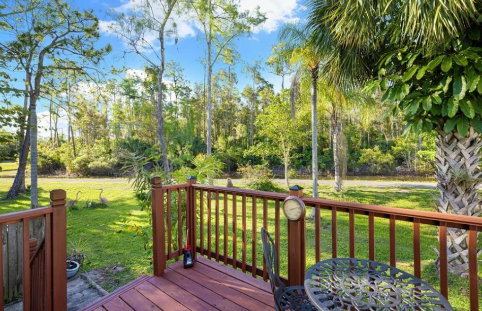 Wooden deck with railing, table, overlooking a grassy yard and trees under a blue sky.