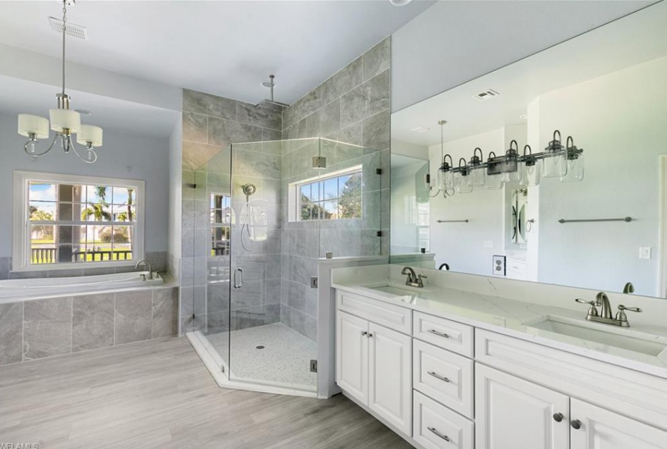 Spacious bathroom with glass shower, white vanity, large mirror, and gray tiled walls.