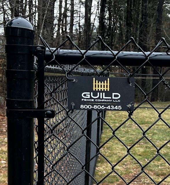 Black chain-link fence with a sign for Guild Fence Company LLC, a company that provides fence services.