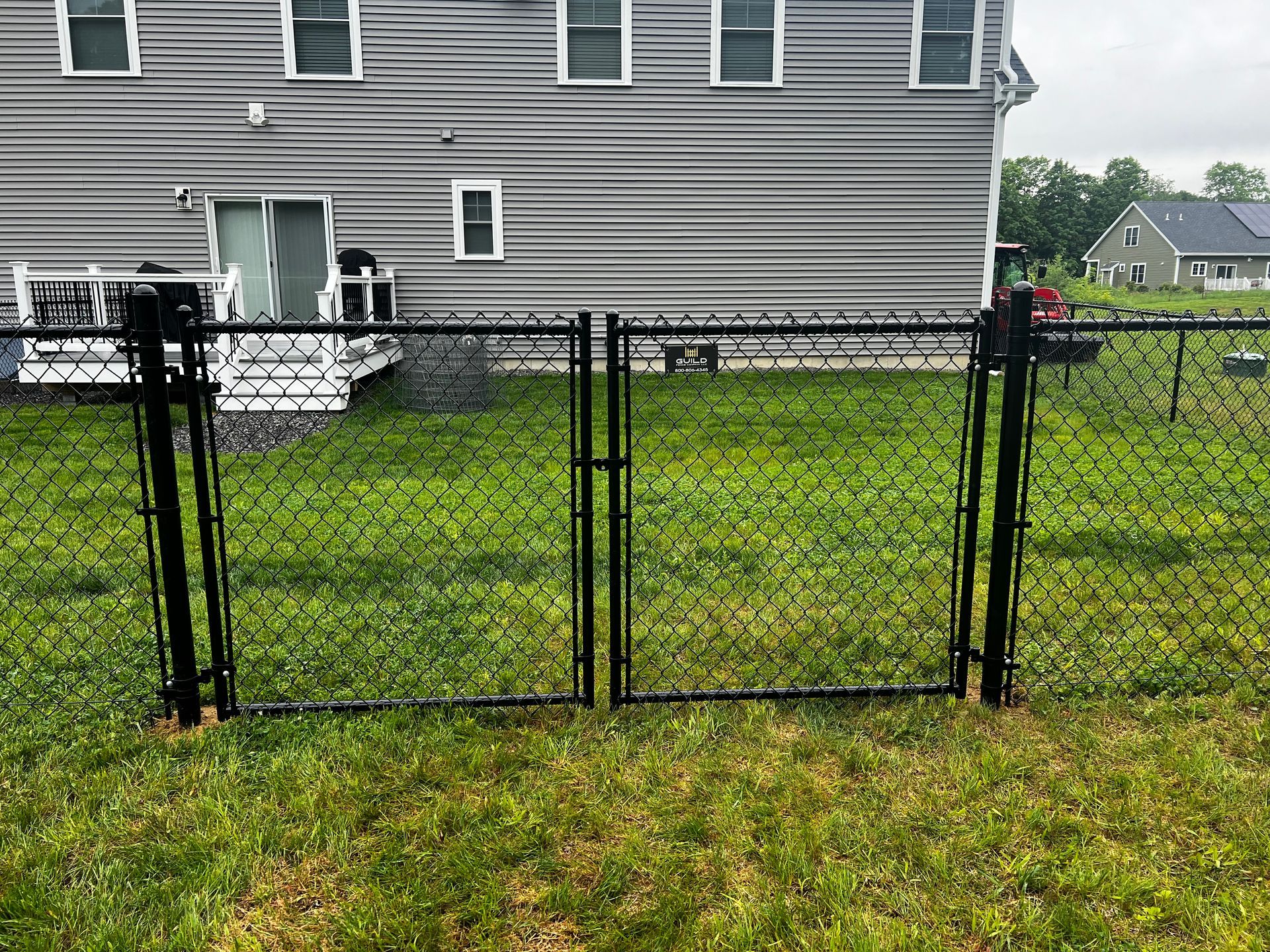 Black chain-link fence with gate in front of a gray house, set in a grassy yard.