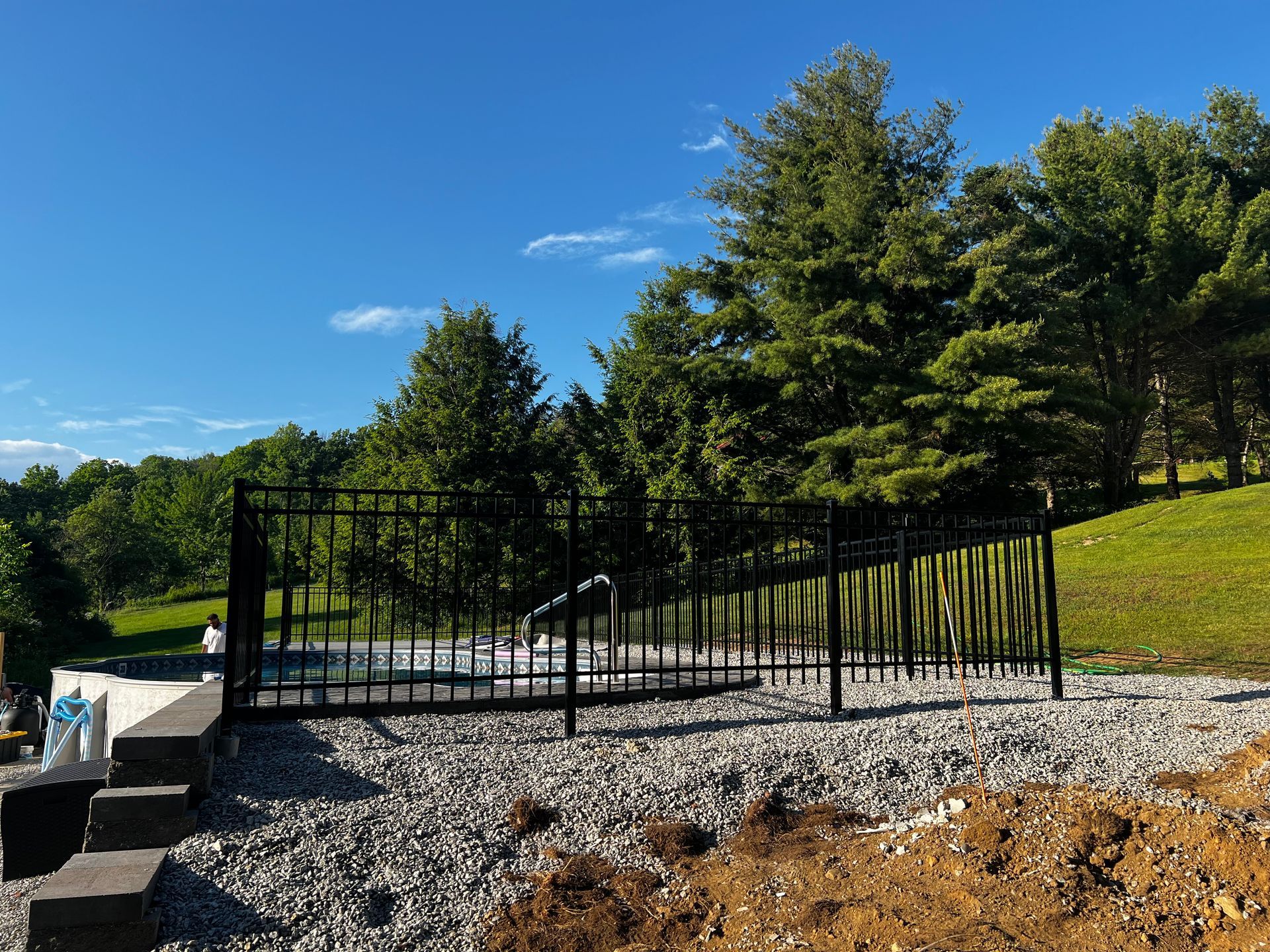 Black metal fence on a gravel bed, with trees and blue sky background.