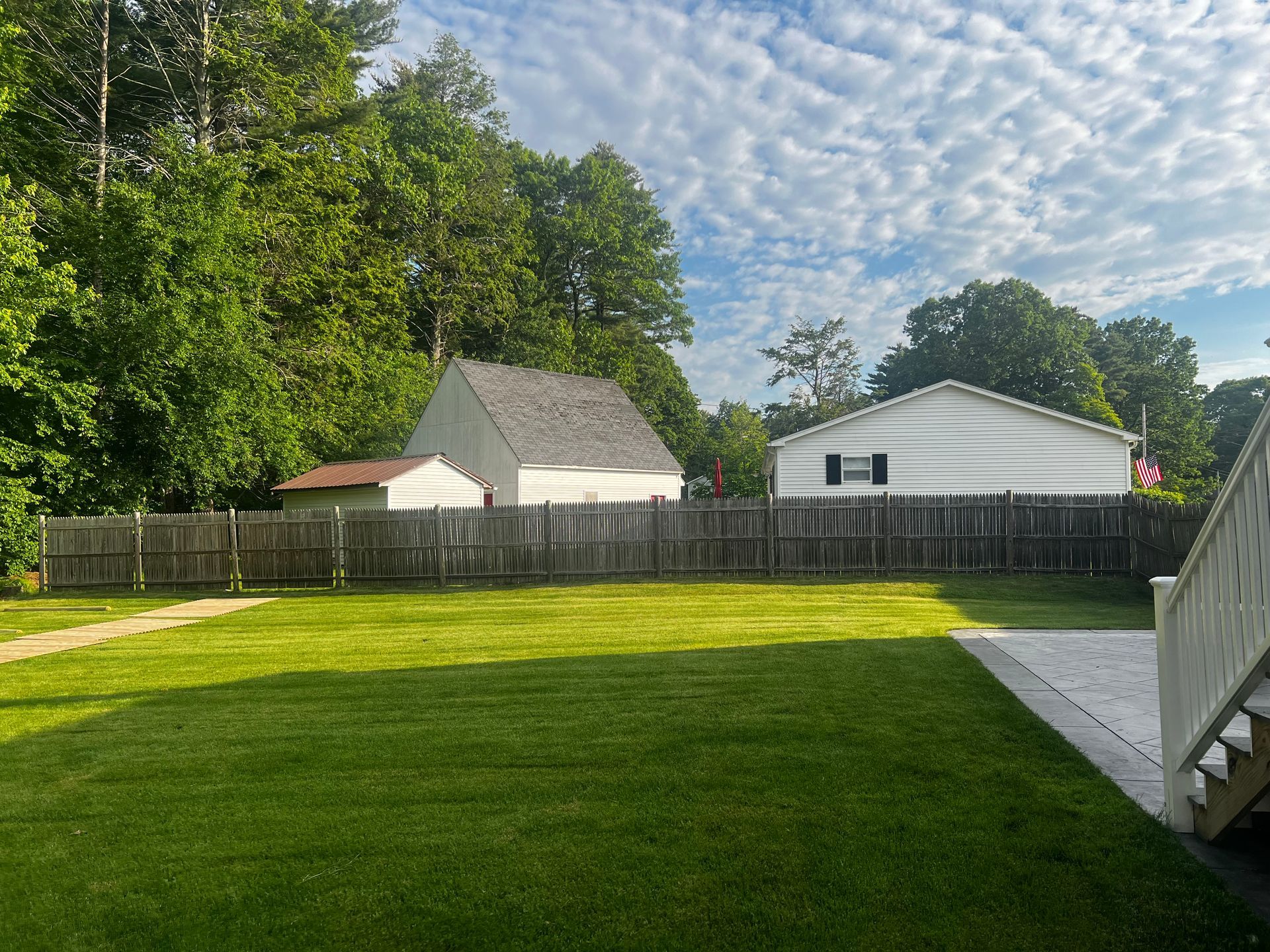 Lawn and fenced yard with two houses under a cloudy sky.